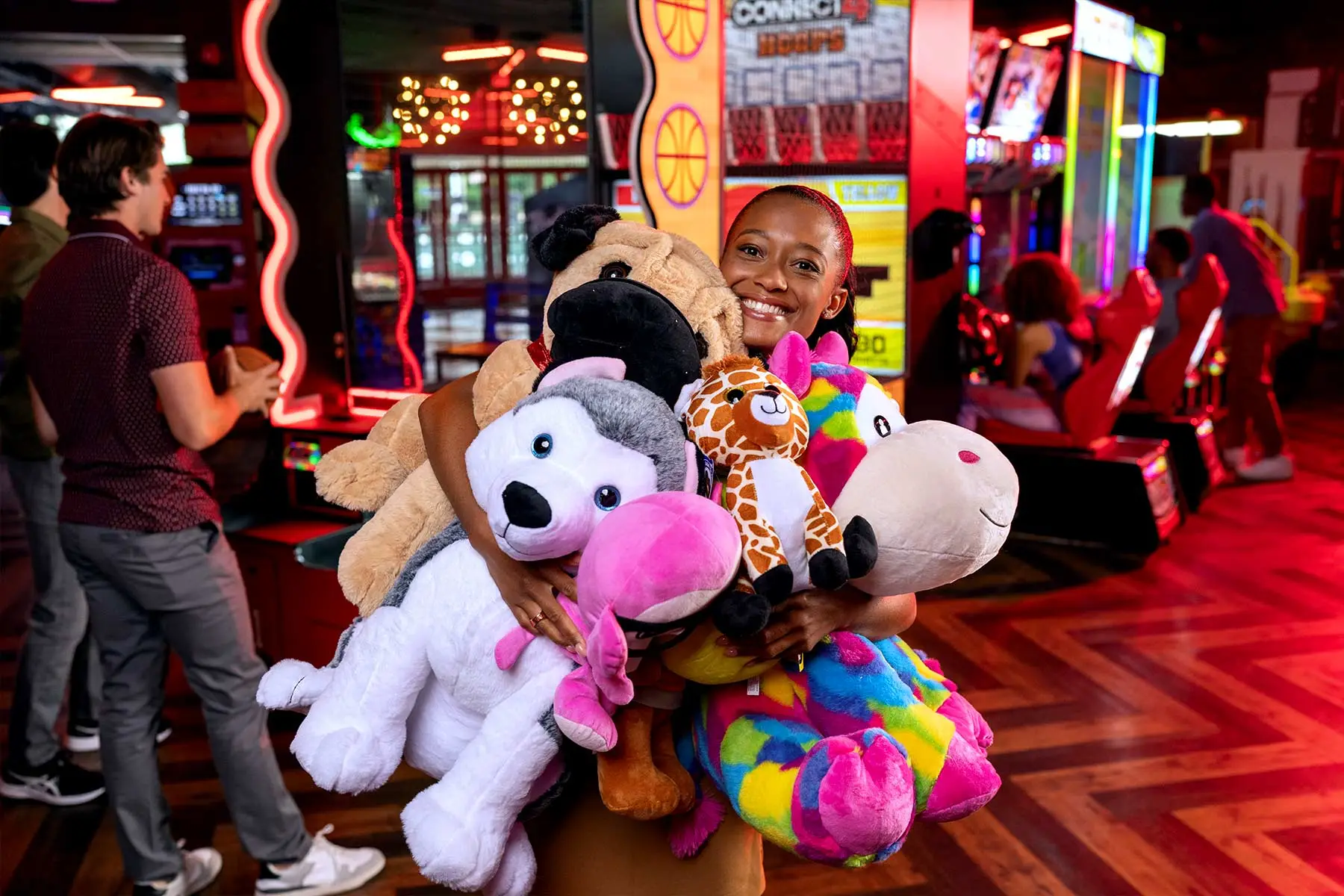 Woman holding lots of large stuffed animals won as prizes with a colorful arcade in the background.