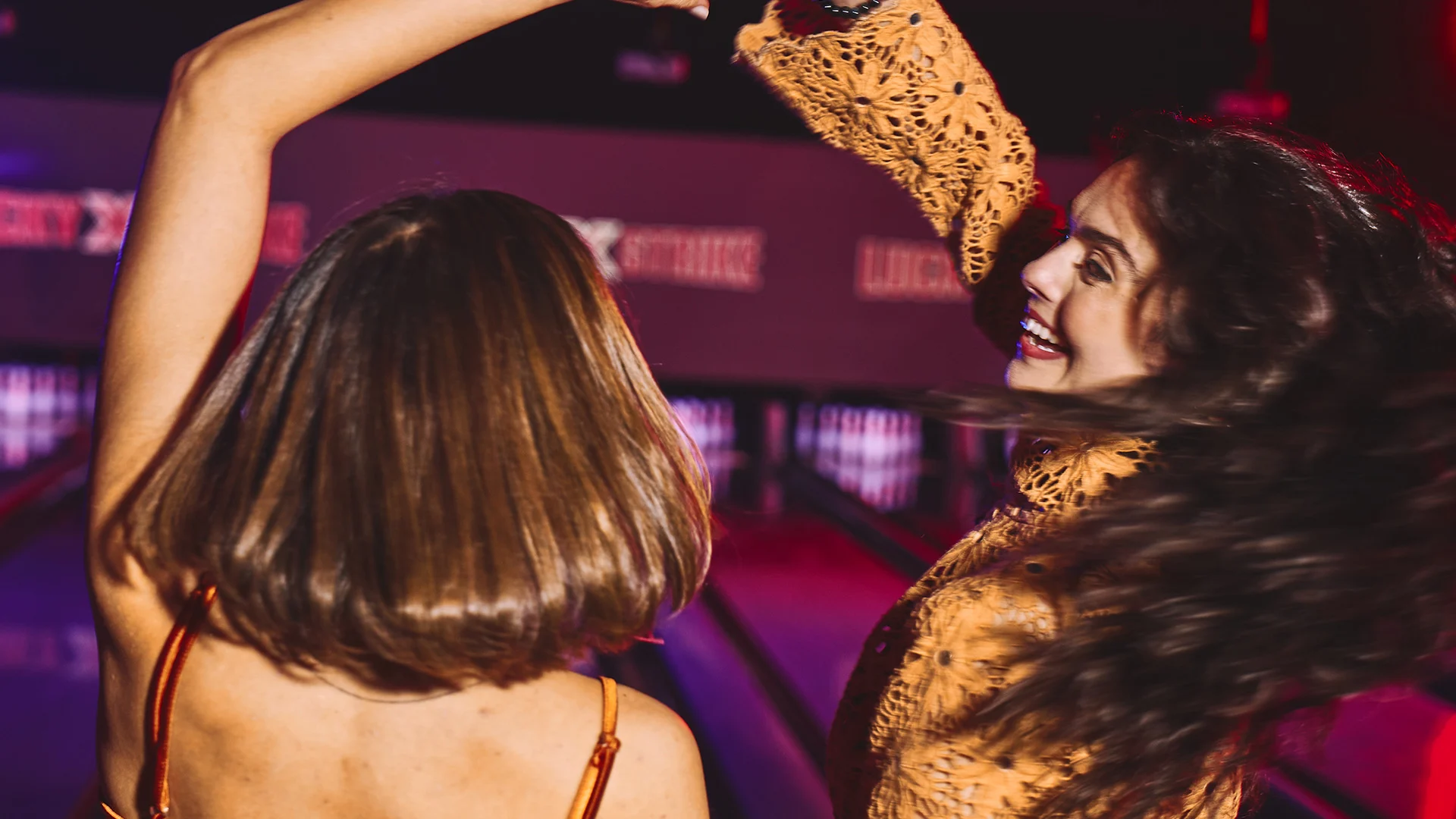 Teenagers dancing and laughing together near bowling lanes during a high-energy group celebration.