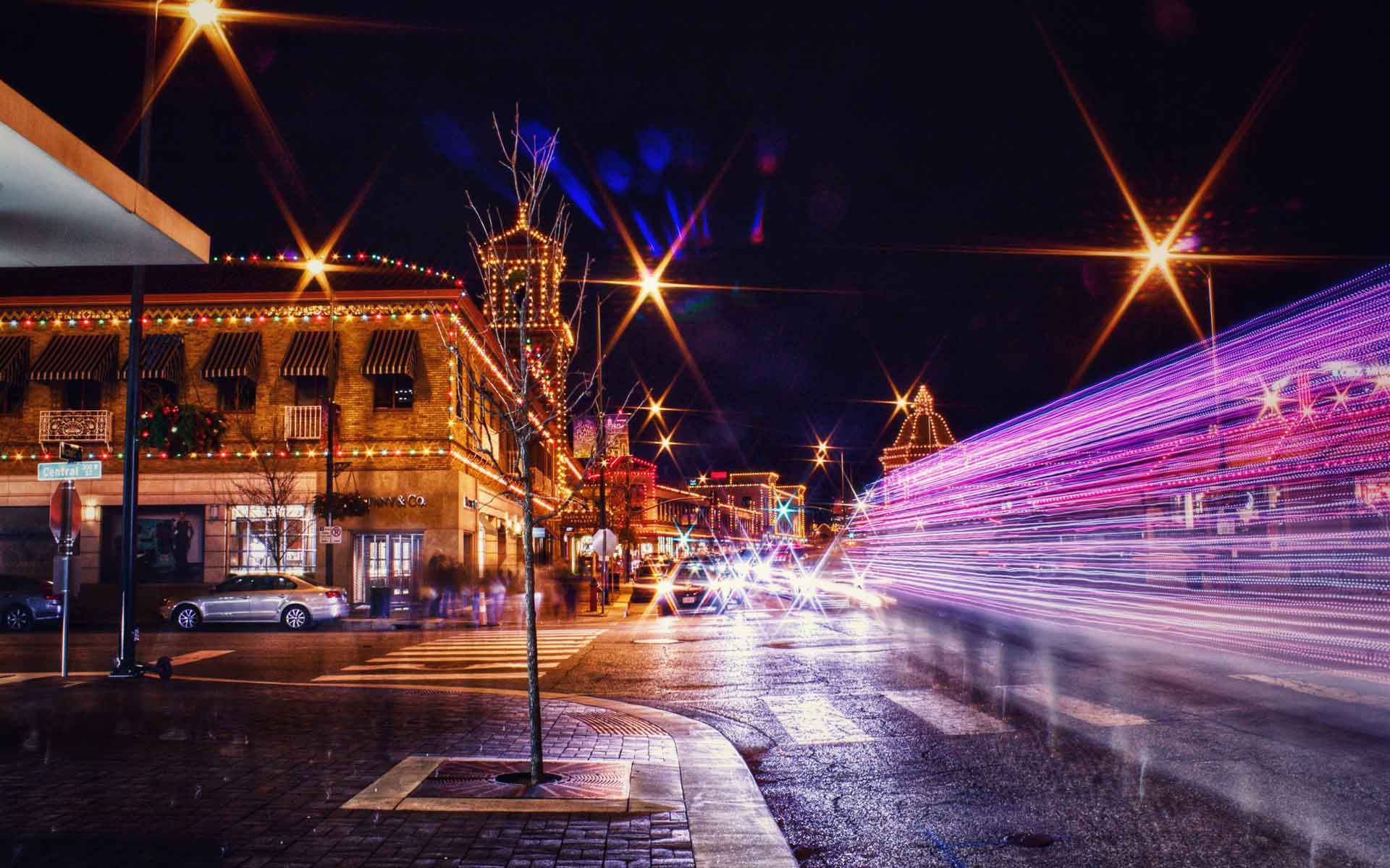 Kansas City nightlife street scene with holiday lights, traffic light trails, and glowing storefronts at night.