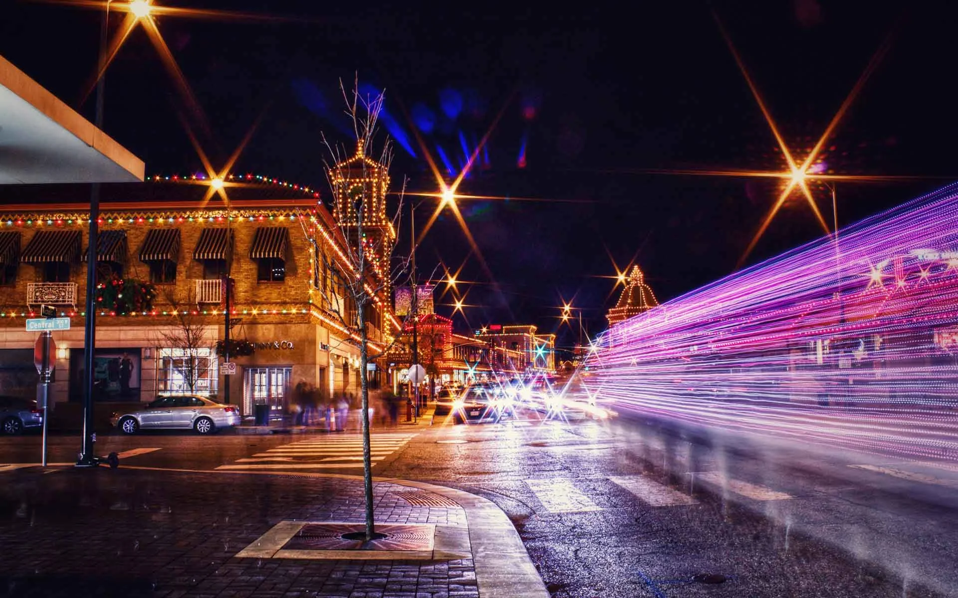 Kansas City nightlife street scene with holiday lights, traffic light trails, and glowing storefronts at night.