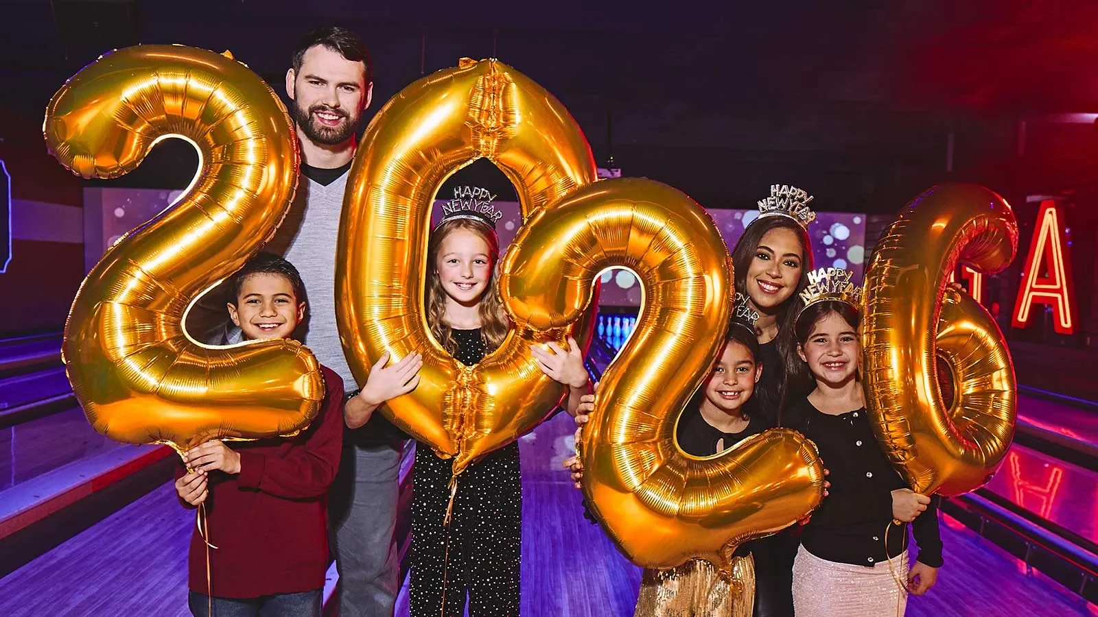 Family with four kids holding up gold 2026 balloons