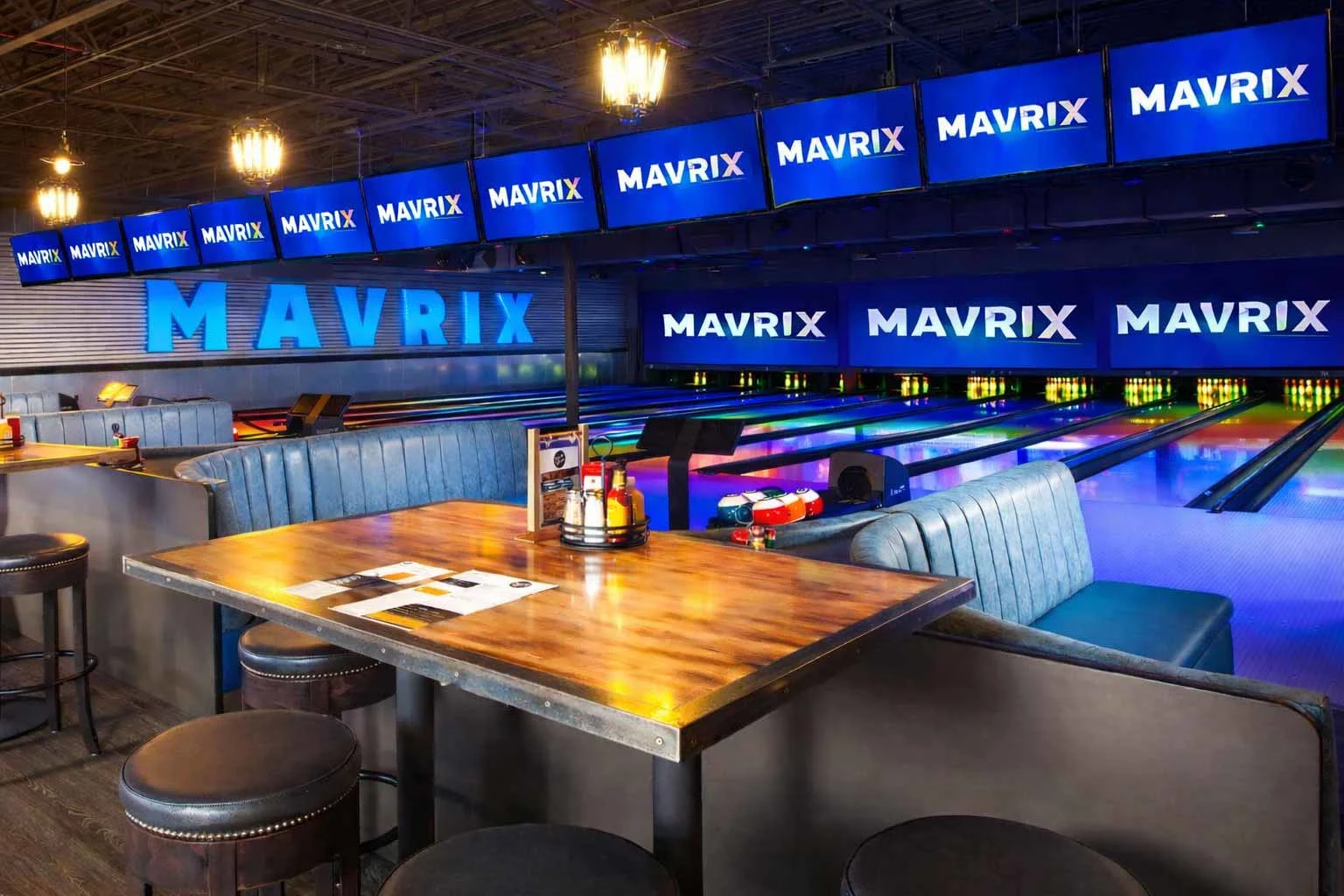 Modern bowling lanes with lounge seating, glowing pins, and upscale dining tables inside Mavrix entertainment center.