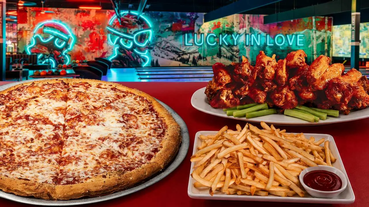 A table filled with delicious party food with bowling lanes and neon signs in the background.