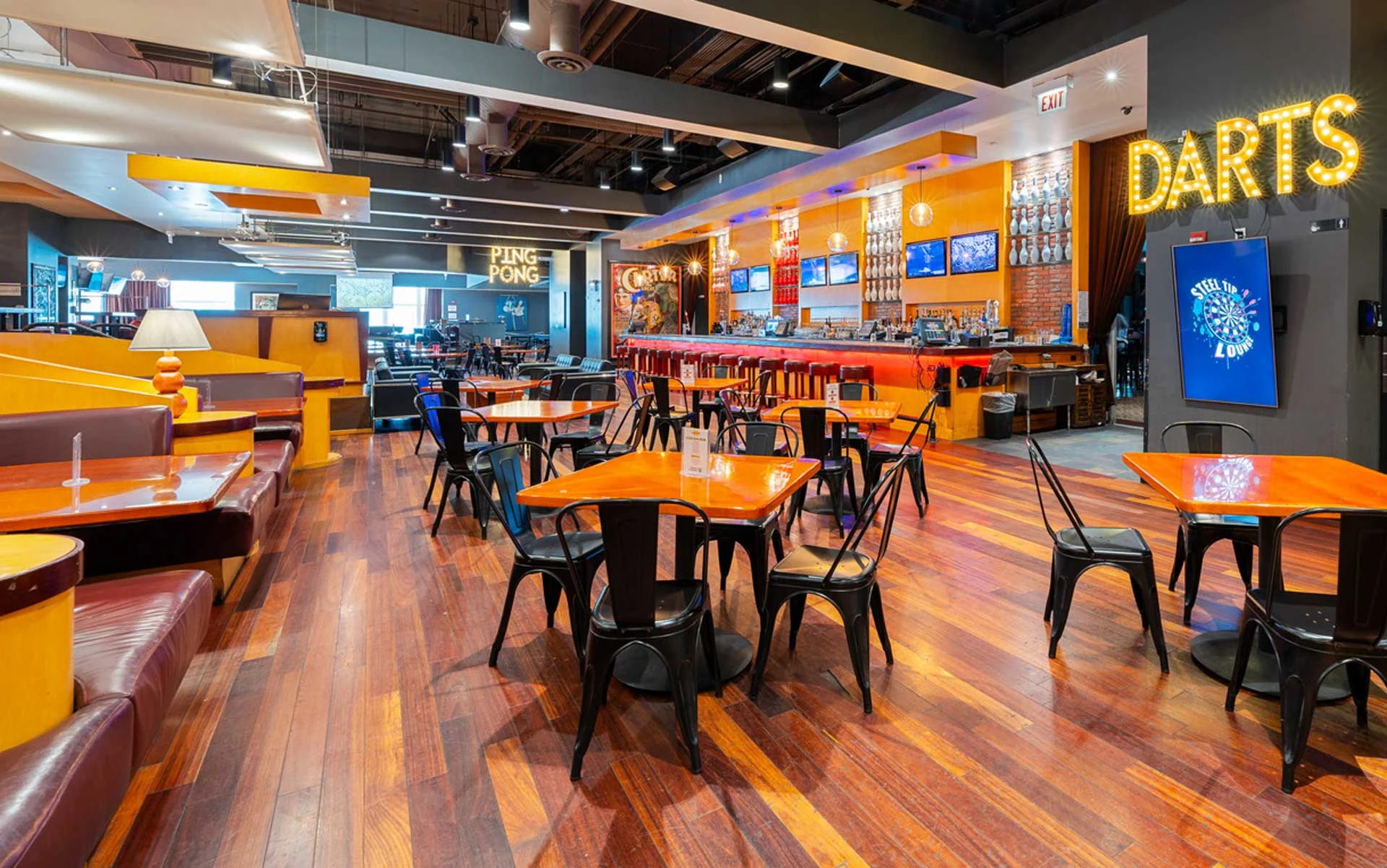 Modern dining and bar space at Lucky Strike with wooden floors, casual seating, glowing bar, and games like ping pong and darts in a social atmosphere.
