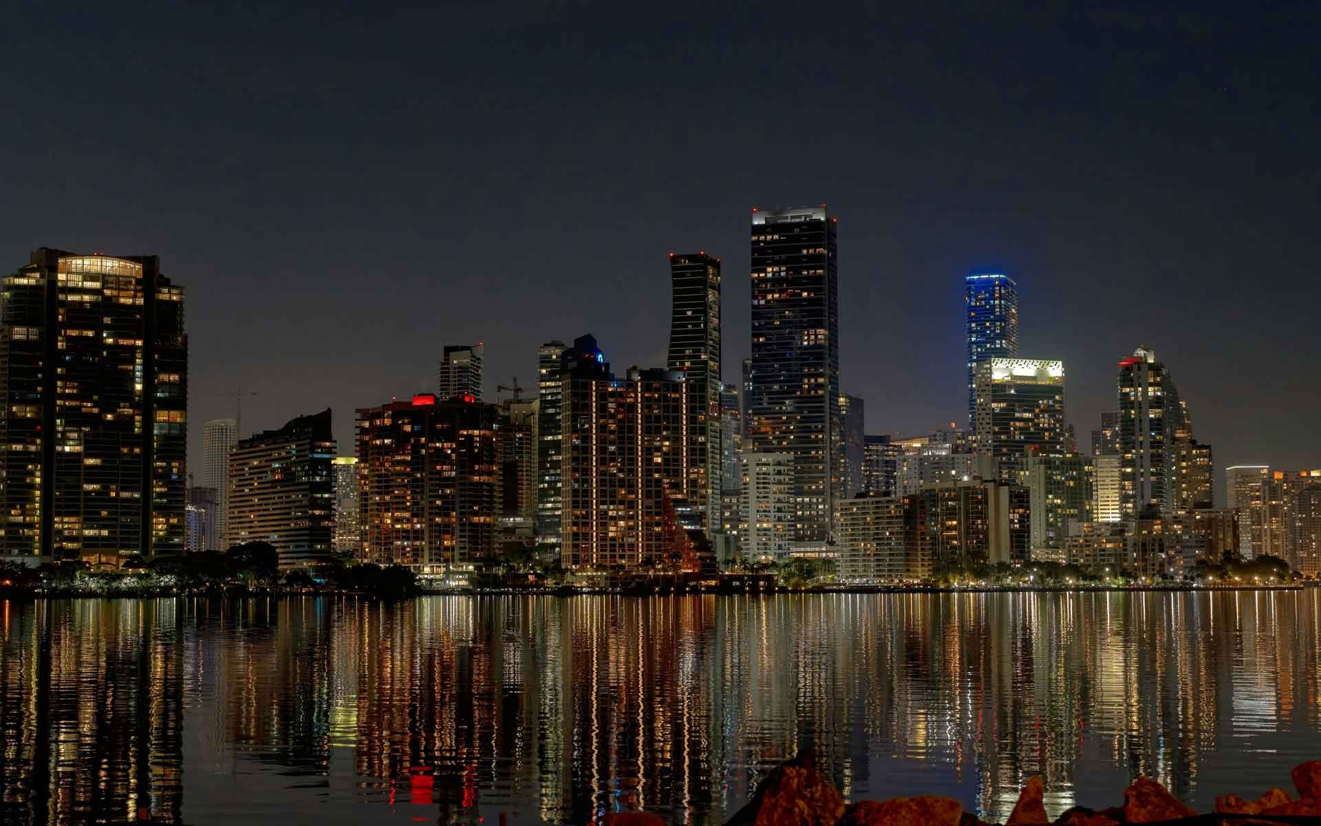 Miami skyline reflected on Biscayne Bay at night with illuminated high-rise buildings and waterfront city lights.