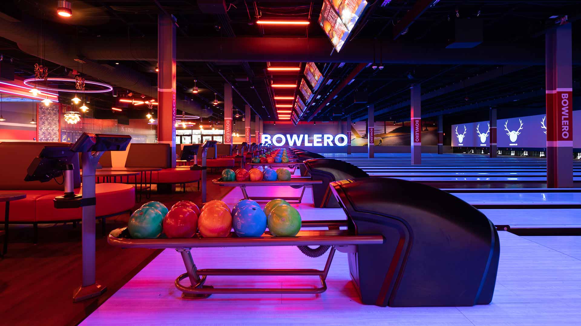 Modern Bowlero bowling lanes with colorful bowling balls, lounge seating, and vibrant neon lighting.