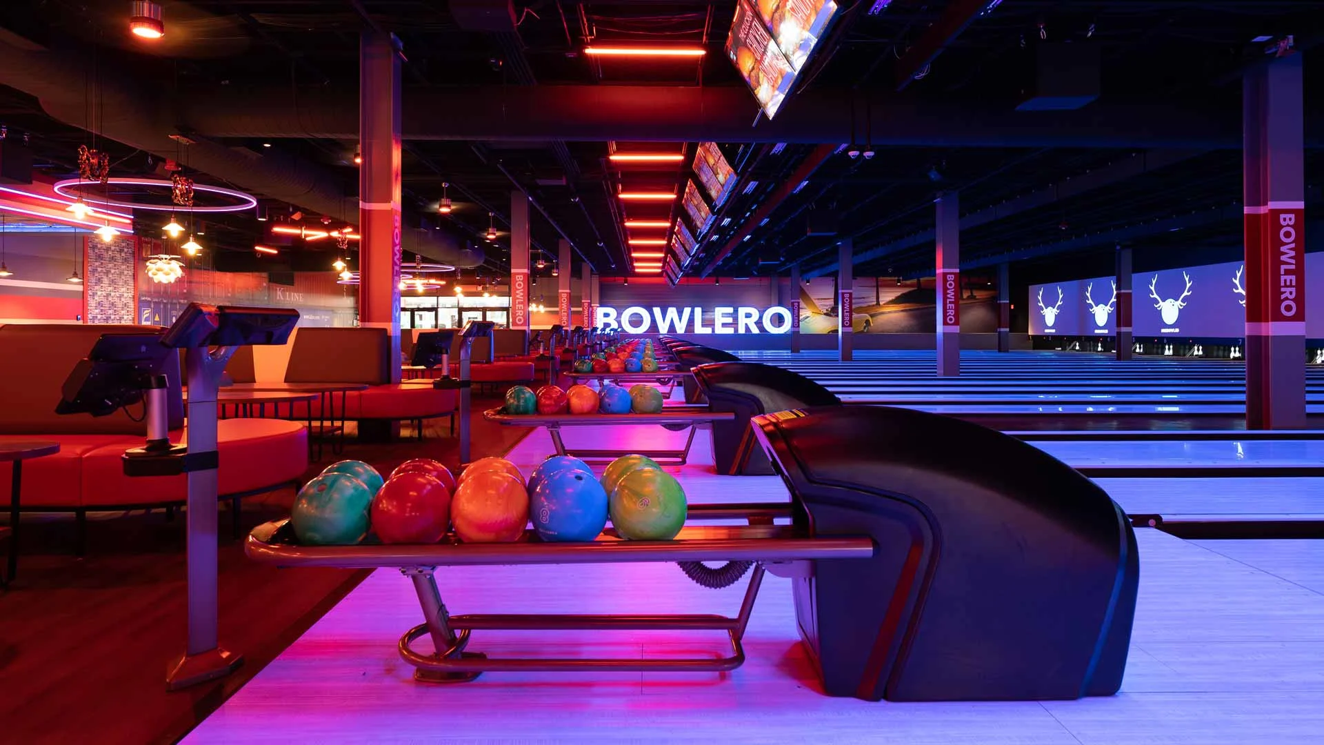 Modern Bowlero bowling lanes with colorful bowling balls, lounge seating, and vibrant neon lighting.