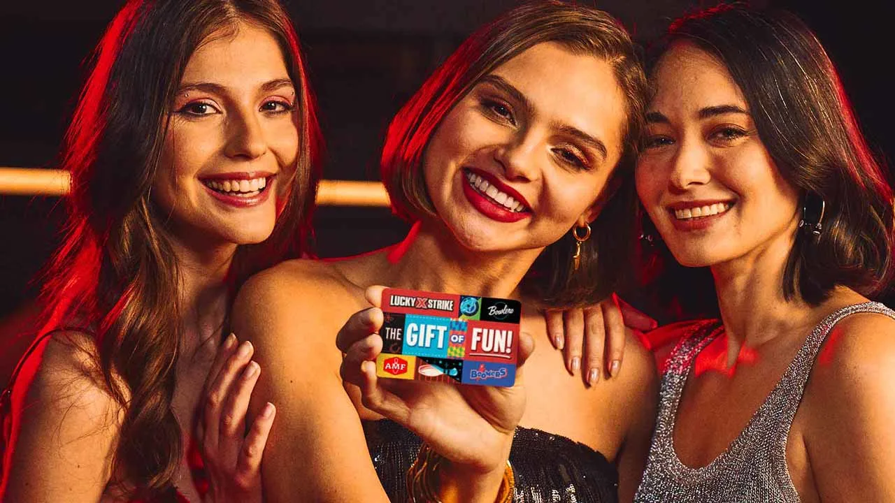 Three women smiling and holding up a Lucky Strike Entertainment gift card.