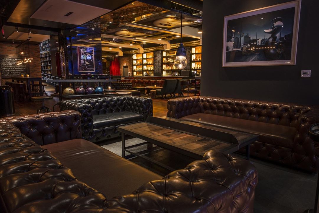 Stylish Lucky Strike lounge with tufted leather sofas, warm bar lighting, bowling ball display, and upscale social seating.