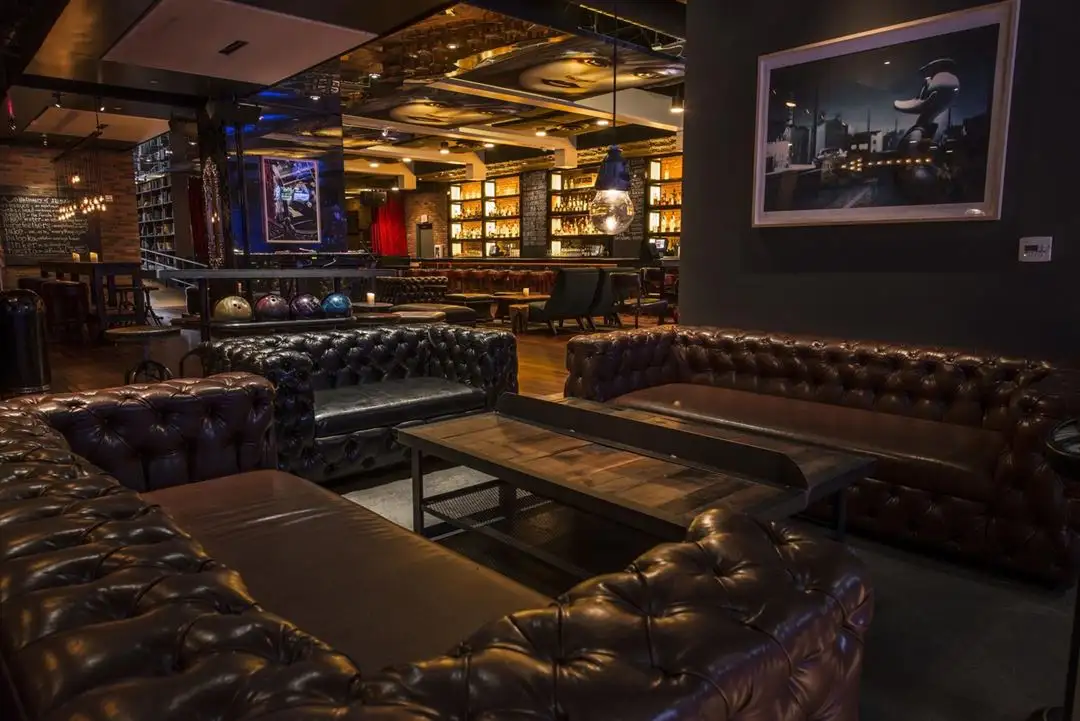 Stylish Lucky Strike lounge with tufted leather sofas, warm bar lighting, bowling ball display, and upscale social seating.