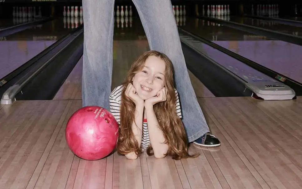 Young girl smiling on the bowling lane beside a pink bowling ball