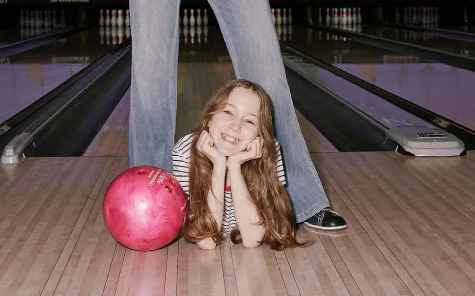 Young girl smiling on the bowling lane beside a pink bowling ball