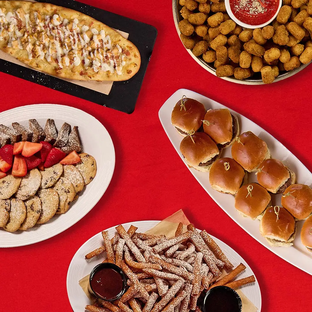 Delicious flatbread, sliders, funnel cake fries, and cookies on a red holiday-themed table