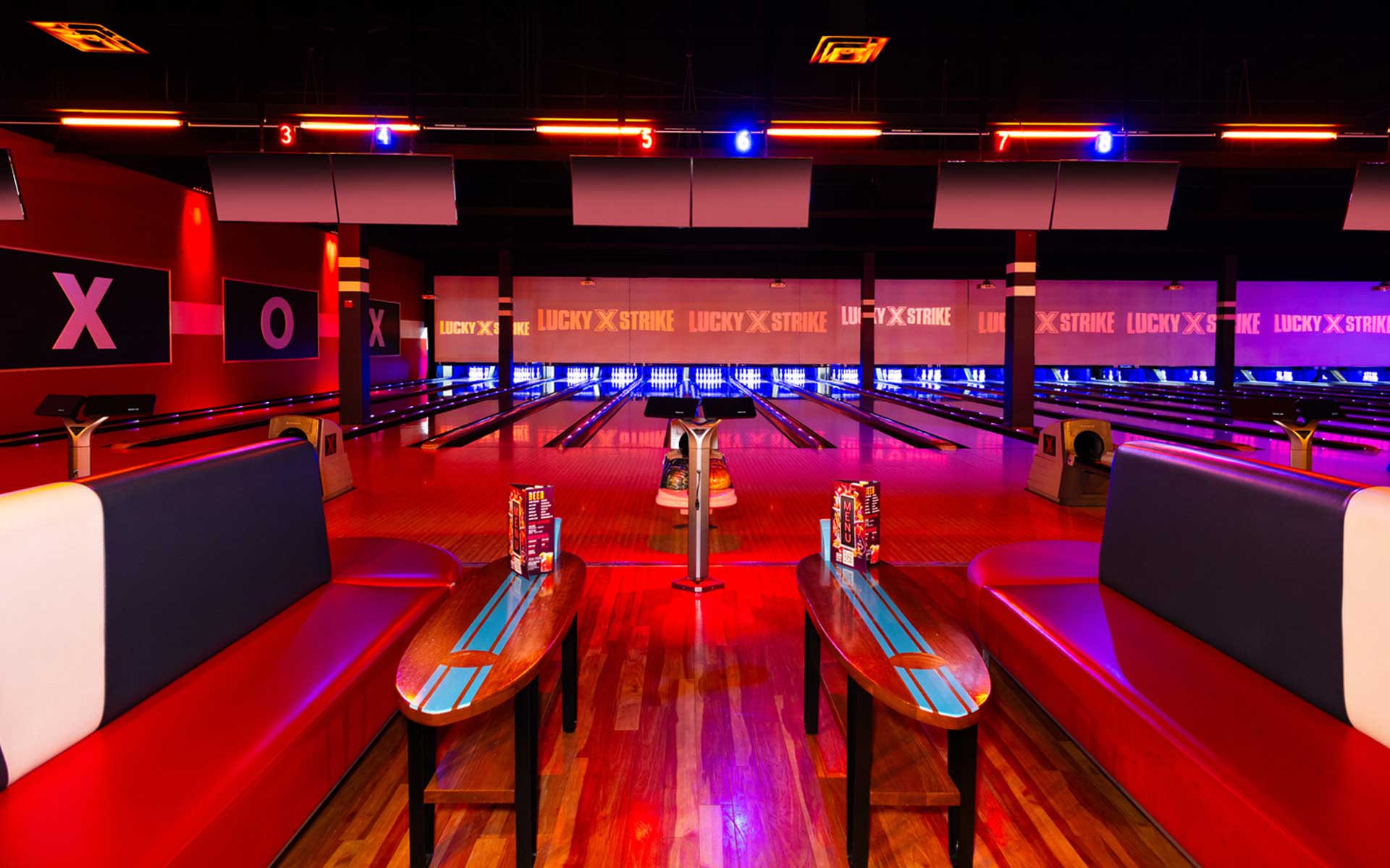 Bowling lanes at Lucky Strike with branded projection screens, glowing lane lighting, and reflections across the polished wood.