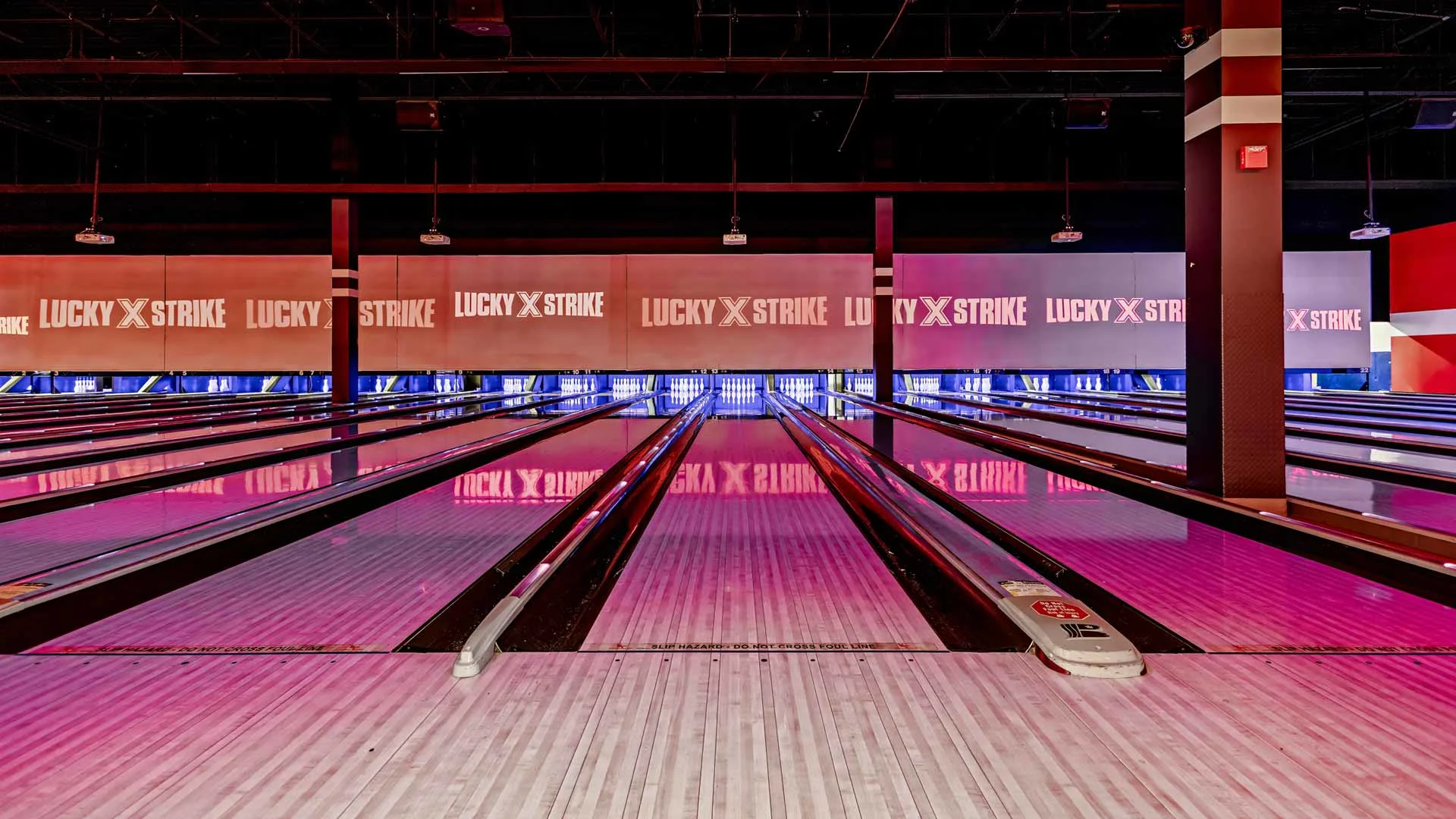 Bowling lanes at Lucky Strike with branded projection screens, glowing lane lighting, and reflections across the polished wood.