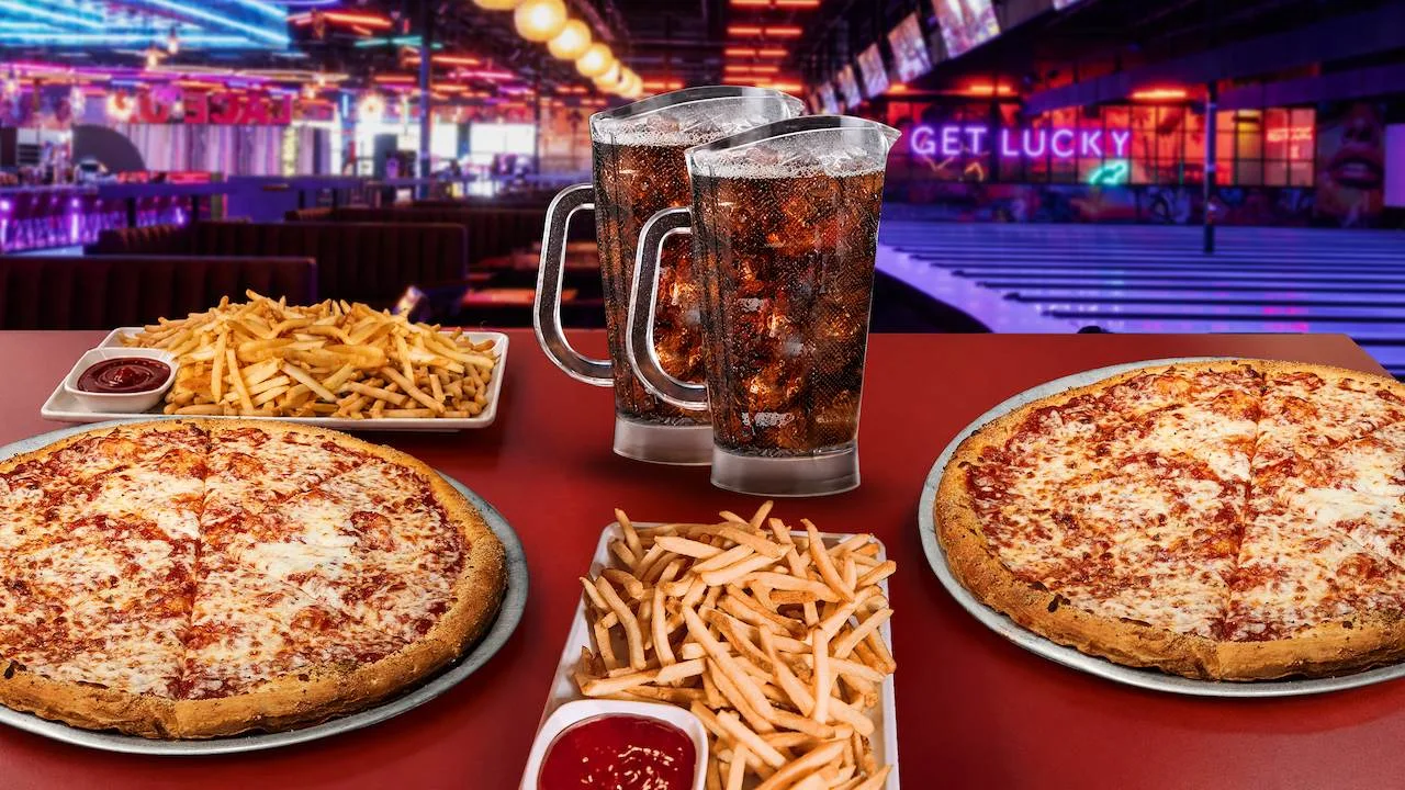 A table filled with delicious party food with bowling lanes and neon signs in the background.