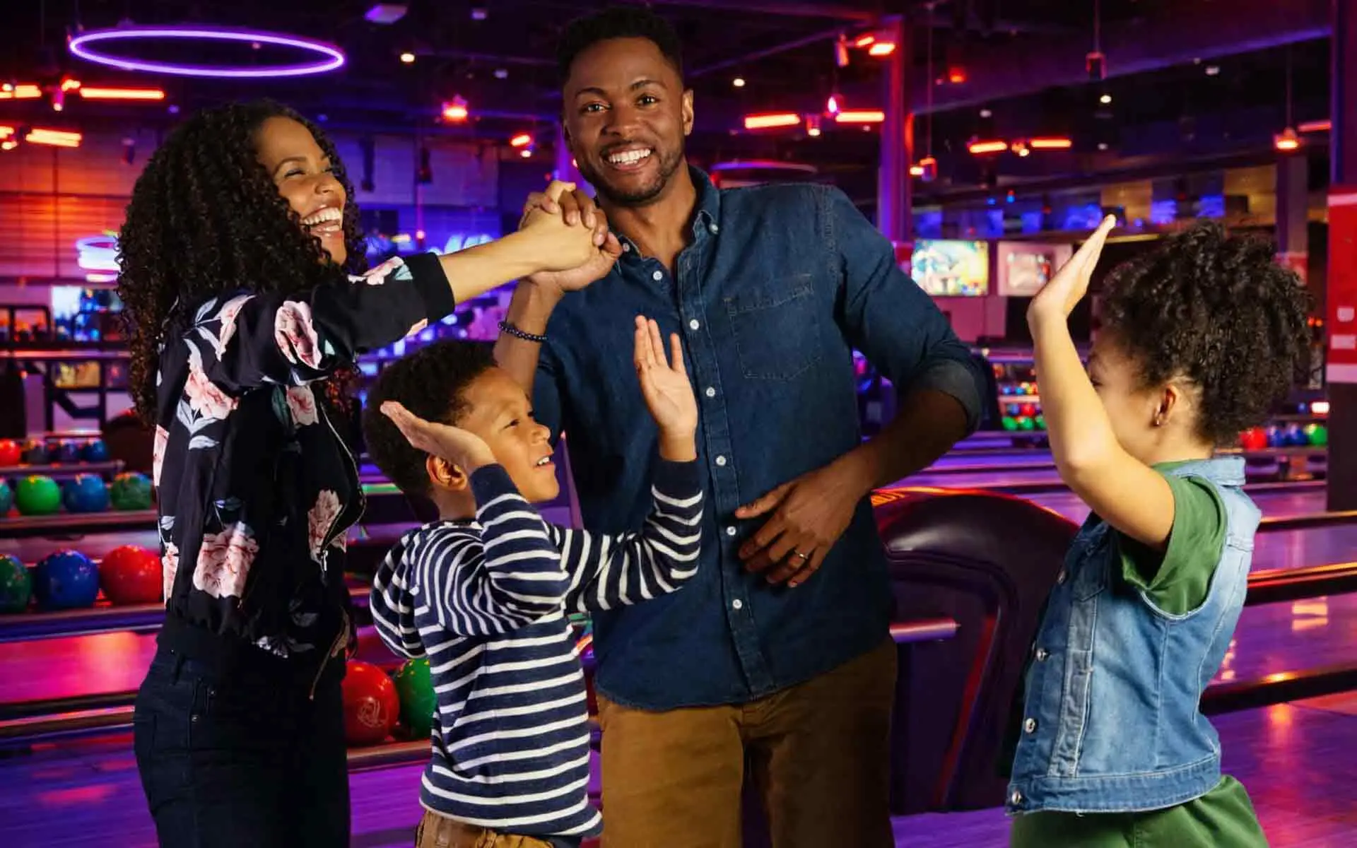 Family celebrating with high-fives at a bowling alley, smiling and enjoying a fun, energetic moment together
