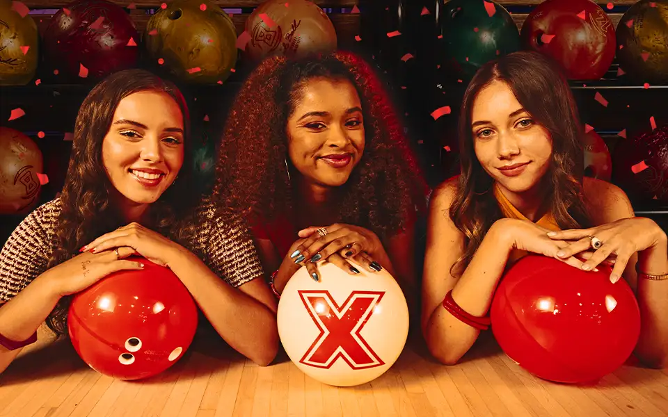 Three women people posing behind red and white bowling balls.