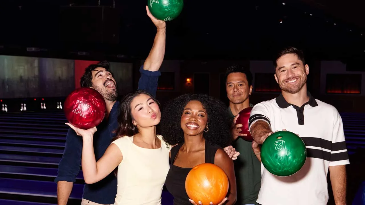 Friend group posing on the approach of a Lucky Strike center with bowling balls.