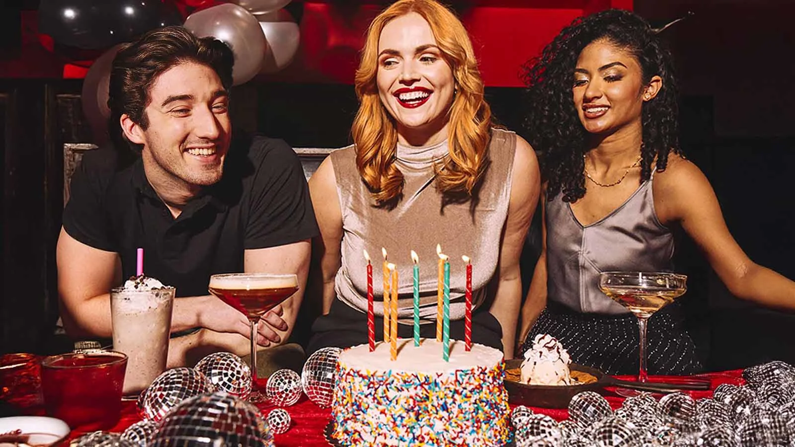 Three people sitting behind a birthday cake with candles.