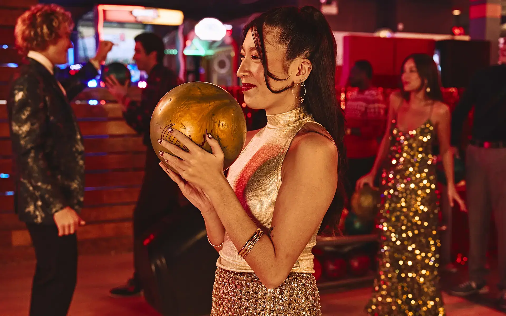 Person holding a bowling ball with a holiday party in the background.