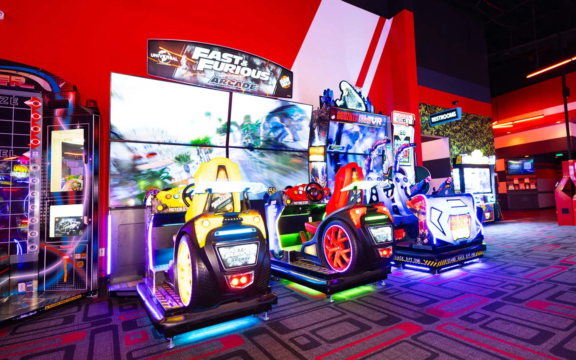 Arcade floor at Lucky Strike featuring Fast & Furious driving games, a Godzilla VR attraction, bright neon lighting, and immersive game displays.