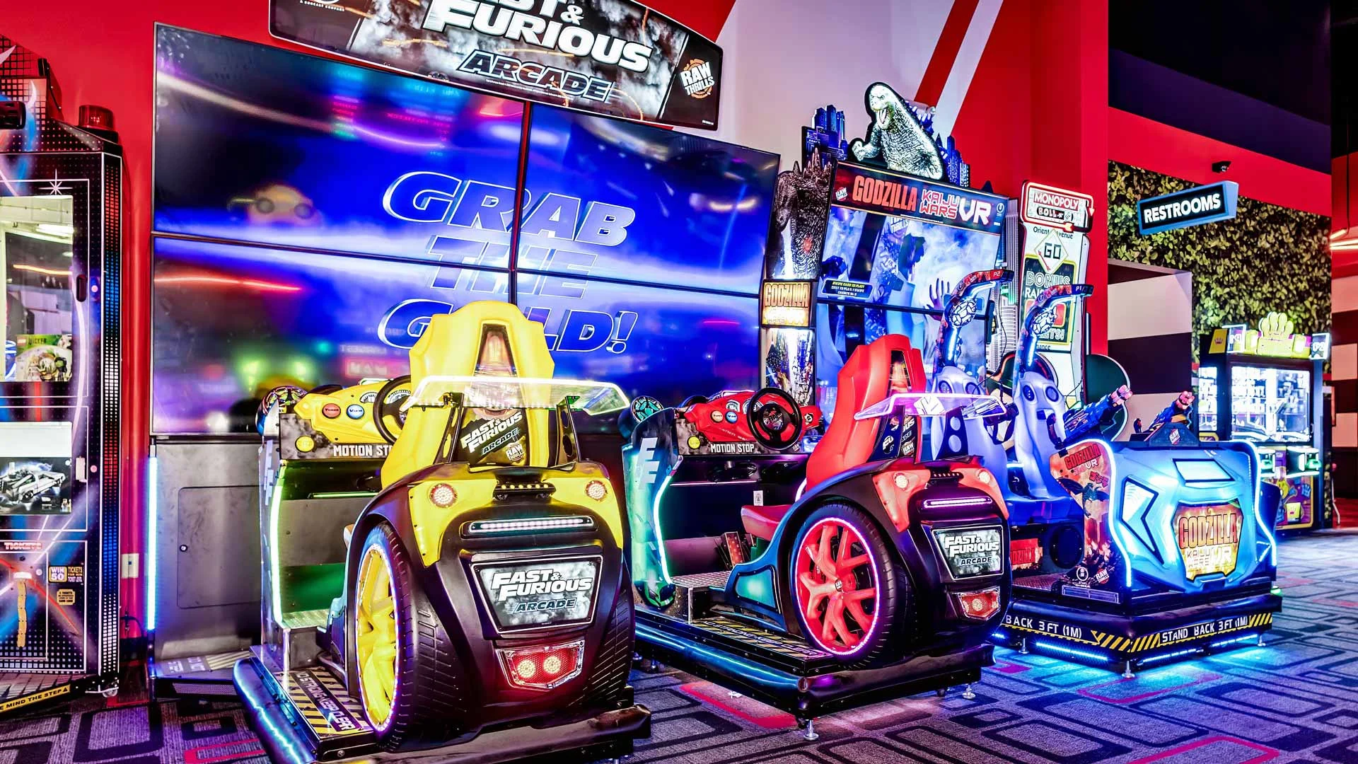Arcade floor at Lucky Strike featuring Fast & Furious driving games, a Godzilla VR attraction, bright neon lighting, and immersive game displays.