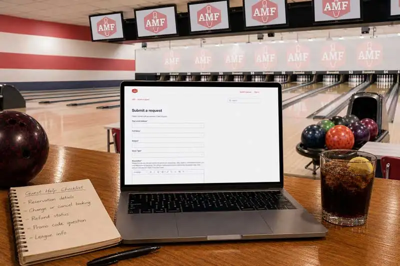 Laptop on a bowling lane table in an AMF center showing a “Submit a request” form, with notepad, drink, lanes, and AMF screens in warm light.