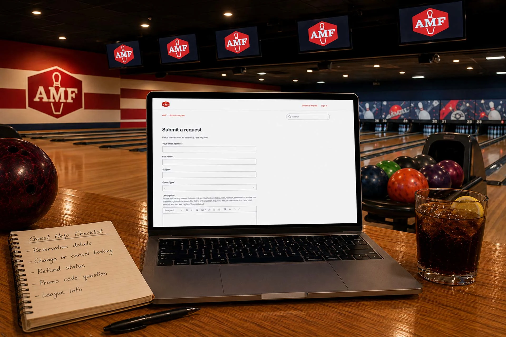 Laptop on a bowling lane table in an AMF center showing a “Submit a request” form, with notepad, drink, lanes, and AMF screens in warm light.