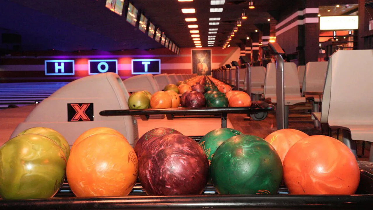 Colorful bowling balls in a return rack with bowling lanes and a bowling center in the background