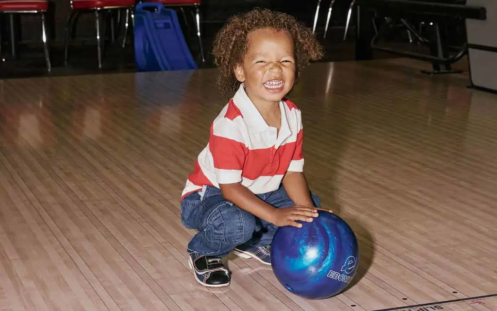Excited toddler crouching with a blue bowling ball at AMF
