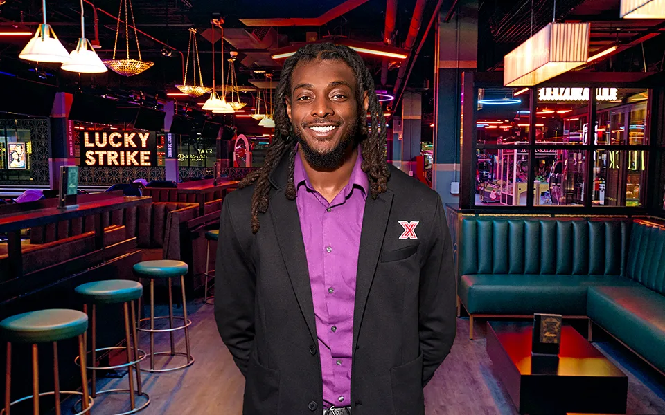 Man with dress jacket with a bar and lounge in the background.