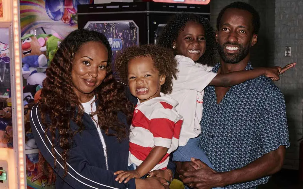 A smiling family of four poses together beside a claw machine in the AMF arcade.
