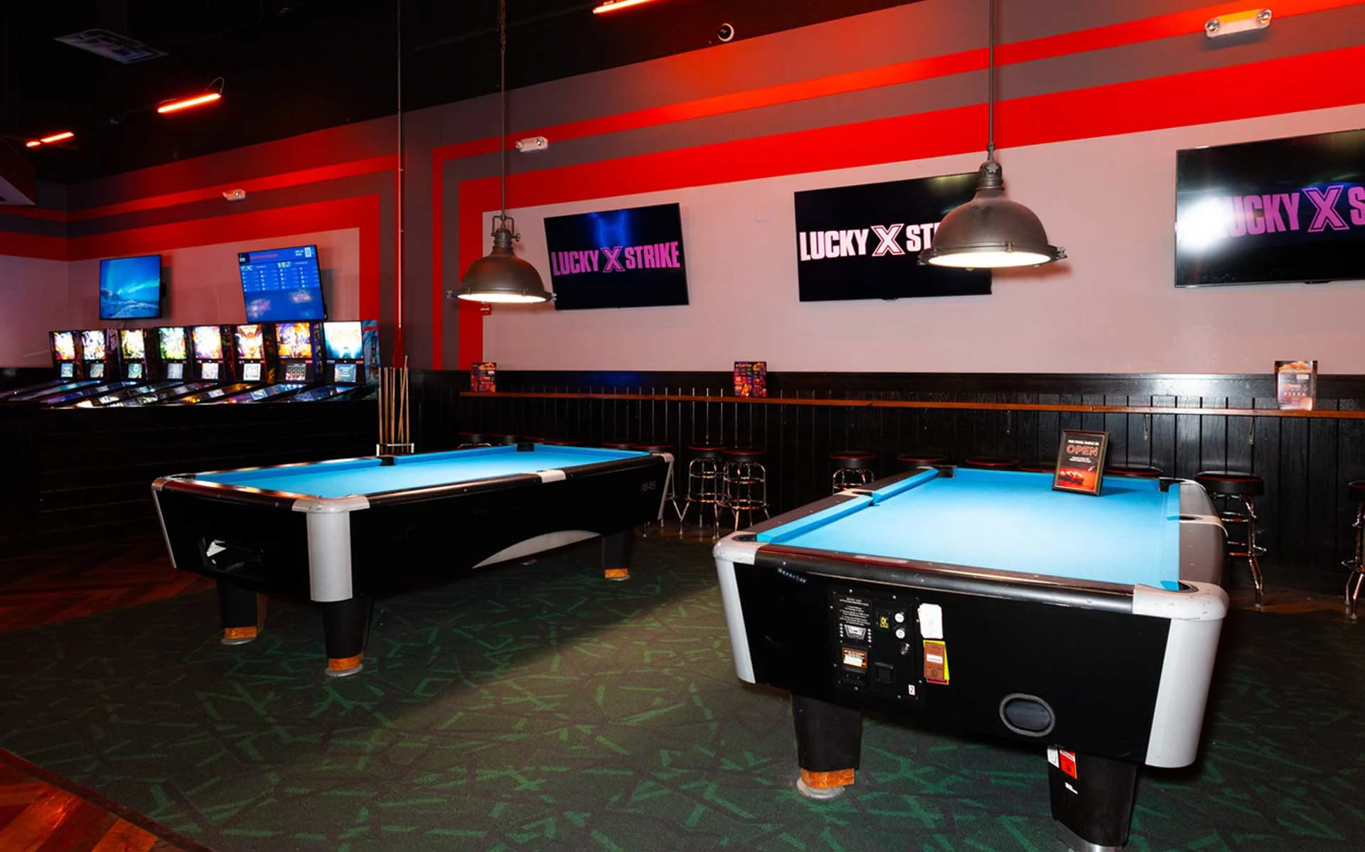 Billiards area at Lucky Strike featuring Brunswick pool tables, lounge seating, wall-mounted screens, and overhead pendant lights.