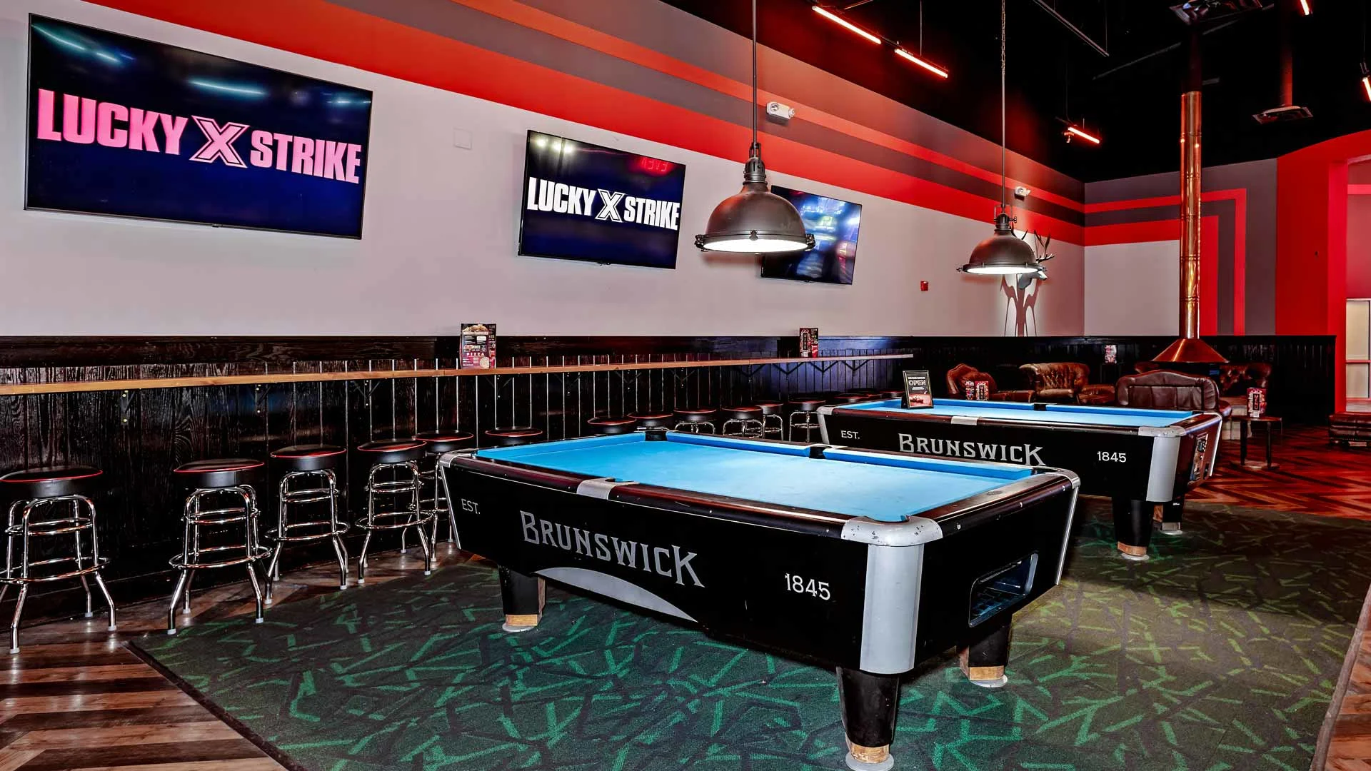 Billiards area at Lucky Strike featuring Brunswick pool tables, lounge seating, wall-mounted screens, and overhead pendant lights.