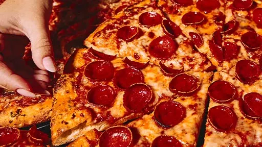 Close-up of a hand grabbing a slice of pepperoni pizza at Lucky Strike, part of the signature food menu.