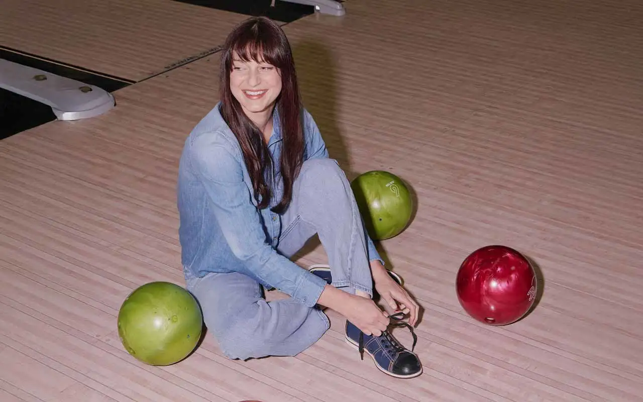 Woman lacing her bowling shoes on the lane beside colorful balls