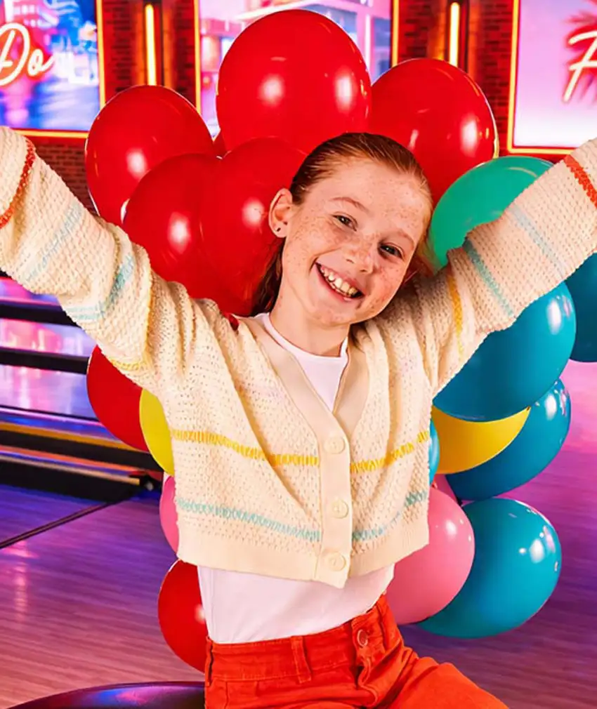 Smiling girl with colorful balloons at a bowling alley birthday party celebration