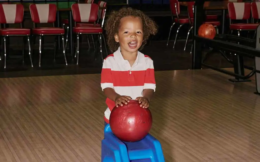 Young child using a bowling ramp to roll a ball at AMF