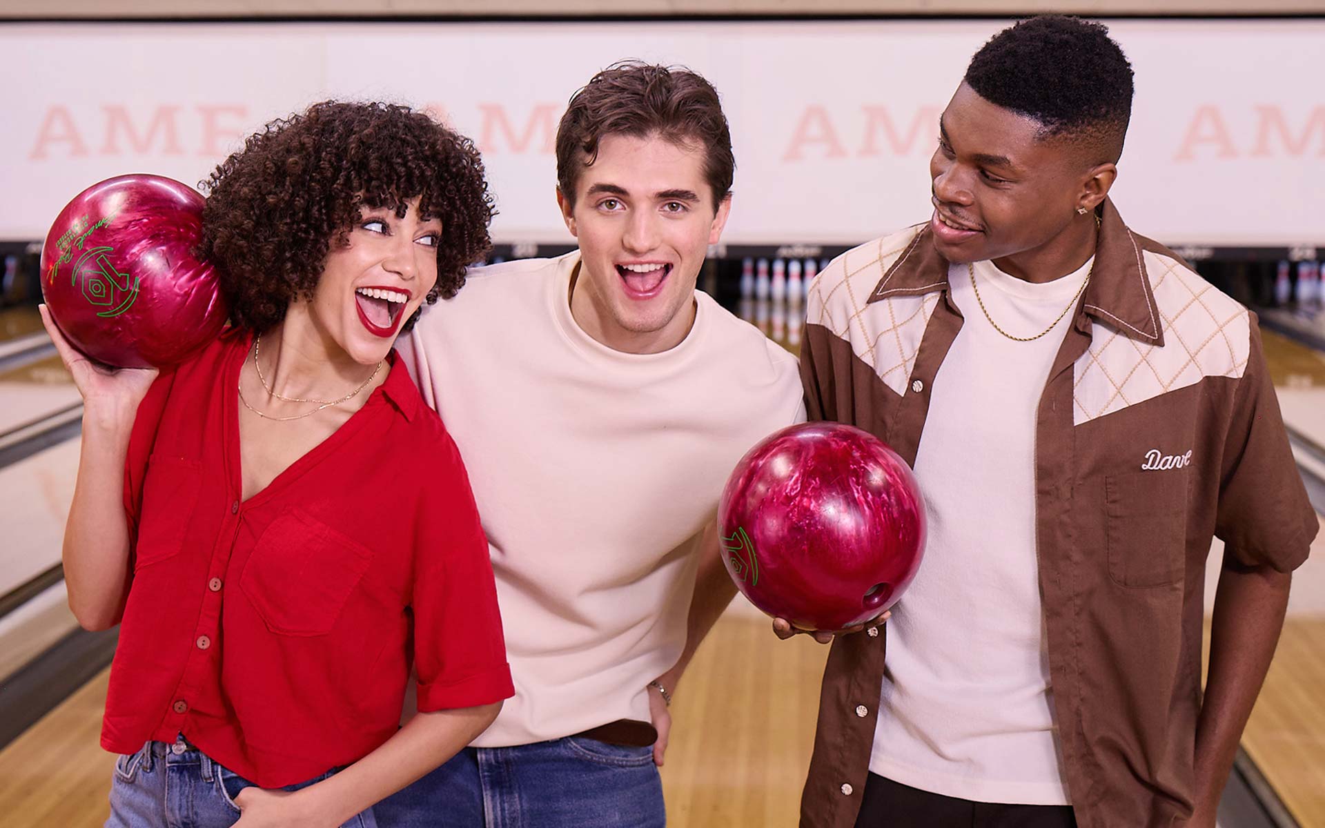 Three friends smiling and holding bowling balls together at AMF bowling lanes.