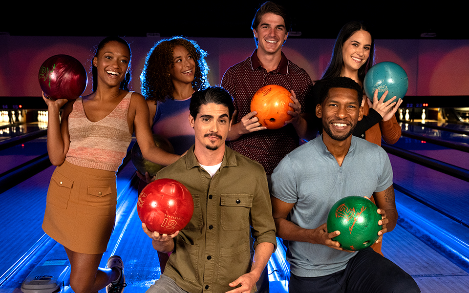 A group of people holding bowling balls posing in front of the lanes