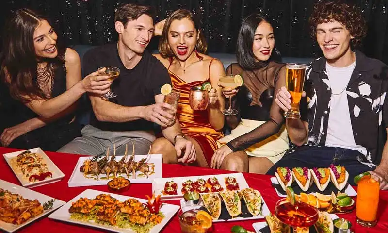 Group of friends enjoying an upscale party with craft cocktails, beer, and shareable appetizers at a Lucky Strike venue, celebrating together with food and drinks in a lively nightlife setting.