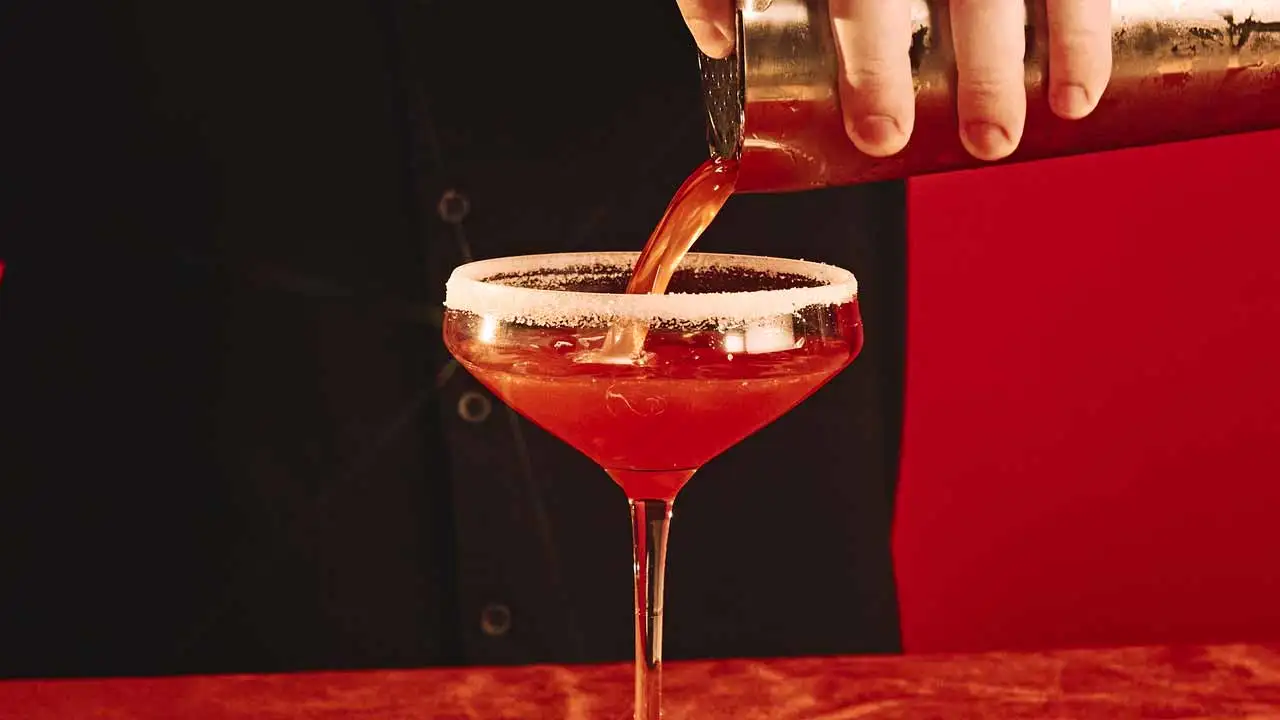 Bartender pouring a cocktail into a sugar rim martini glass.