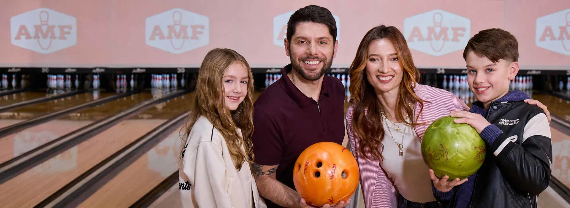 Family smiling with bowling balls at AMF, standing in front of bowling lanes with pins and AMF logos in the background.