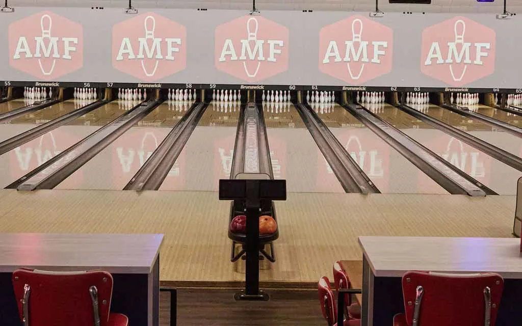 Freshly conditioned AMF bowling lanes with pins set and ball returns ready, framed by the AMF logo wall and diner-style seating.