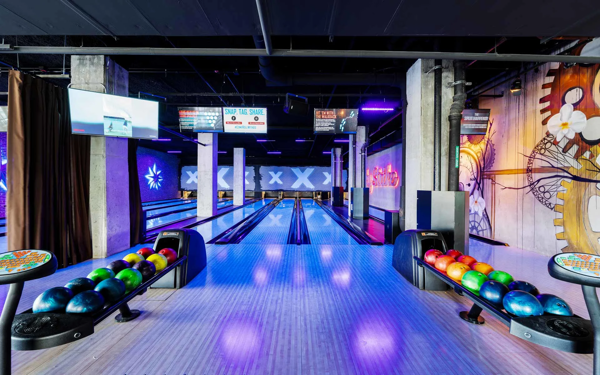 Modern bowling lanes with glowing neon lighting, ball returns, and digital screens inside a Lucky Strike bowling center.