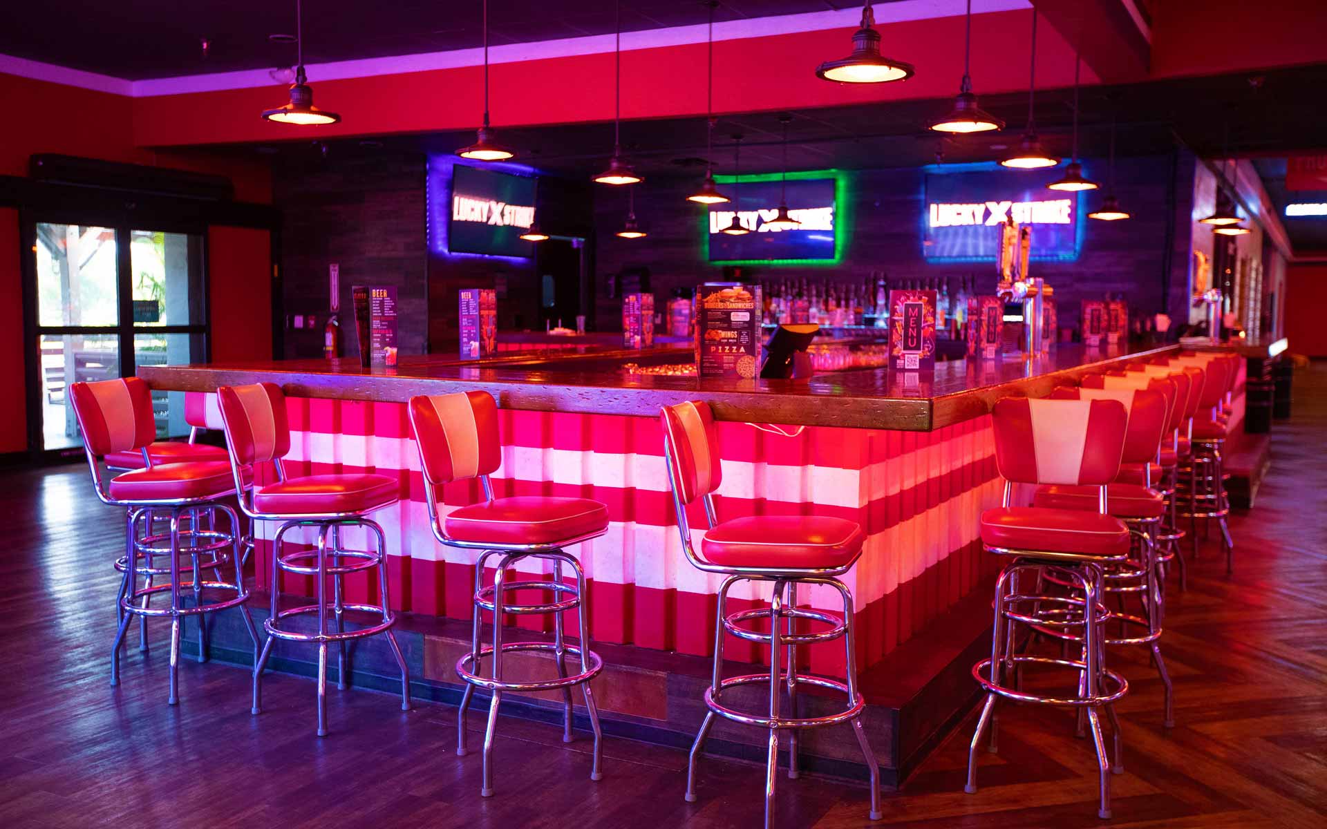 Lucky Strike bar area with red bar stools, glowing LED accents, and multiple screens in a modern bowling lounge.