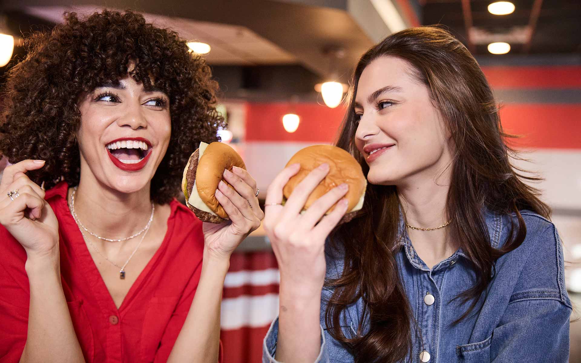 Two women enjoying burgers and laughing together at an AMF bowling alley.
