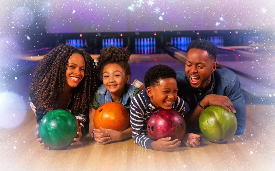 Four bowlers posing with bowling balls with bowling lanes in the background.