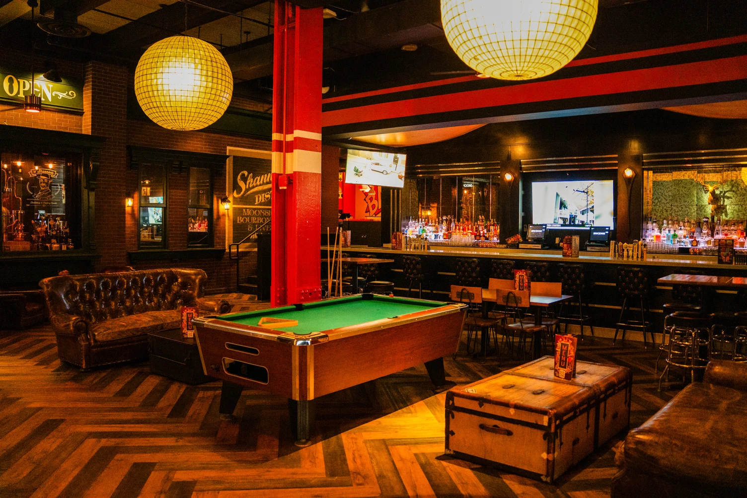 Pool table and full bar area inside Lucky Strike Times Square entertainment venue with globe pendant lighting and herringbone wood floors